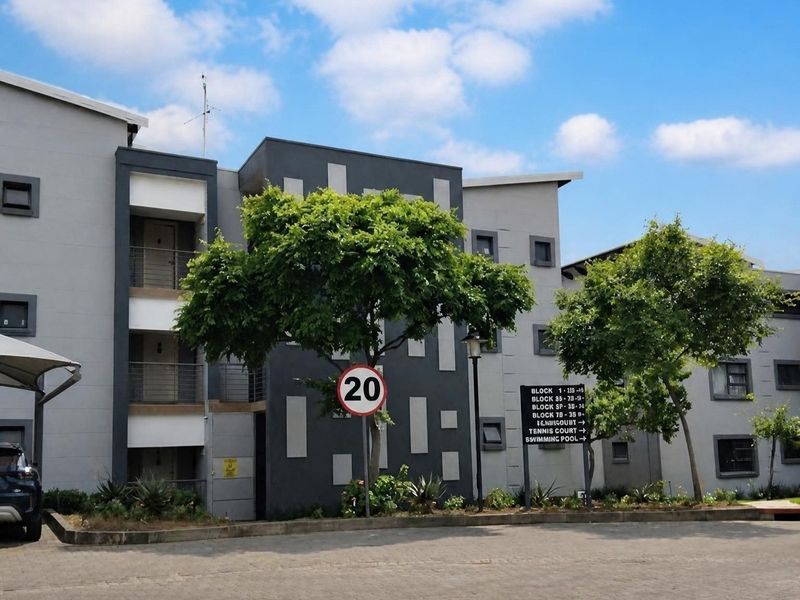 Exterior view of a modern apartment complex featuring a paved driveway, directional signage, and well-maintained building facades.