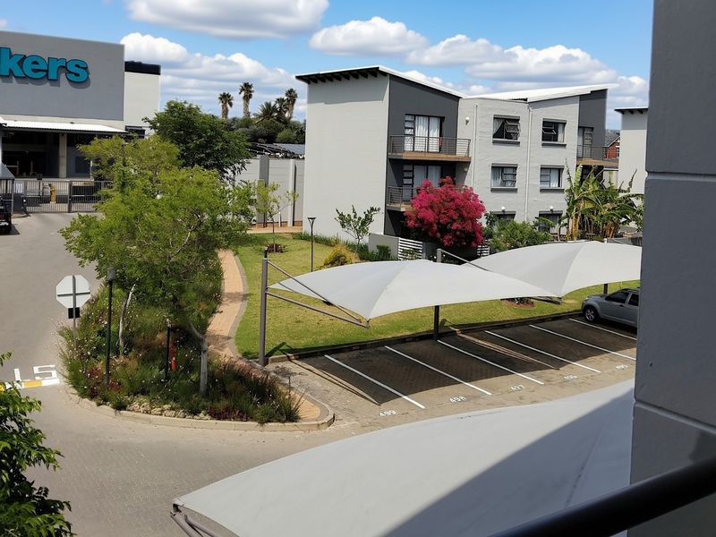 Elevated view overlooking a well-maintained apartment complex, featuring paved parking bays with shade cloth carports and landscaped garden areas.