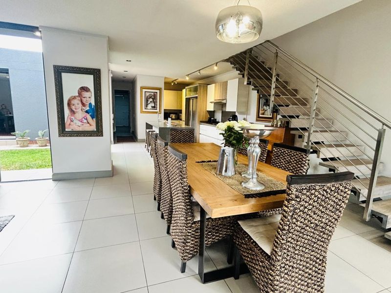 Spacious open-plan living and dining area featuring modern tiled floors, a contemporary staircase with stainless steel balustrades, and seamless access to the outdoor patio.