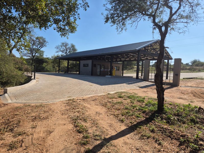 A modern security gatehouse featuring a paved driveway, metal roof structure, and integrated boom gate access control for the residential estate.