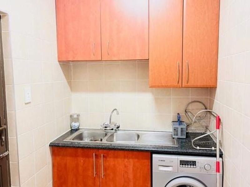 A functional laundry area featuring laminate cabinetry, a double basin stainless steel sink, granite countertops, and tiled walls with integrated washing machine plumbing.