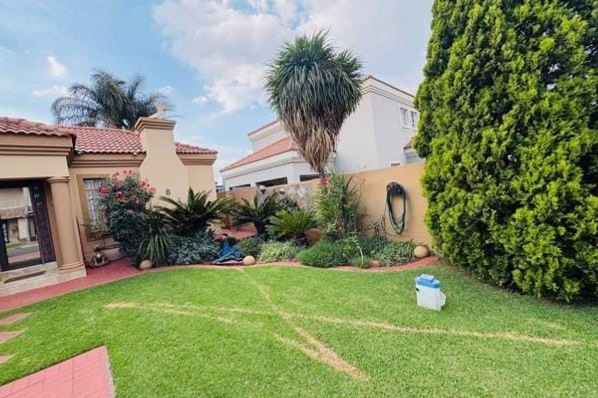 A well-maintained rear garden area featuring a manicured lawn, paved pathways, and established perimeter boundary walls.