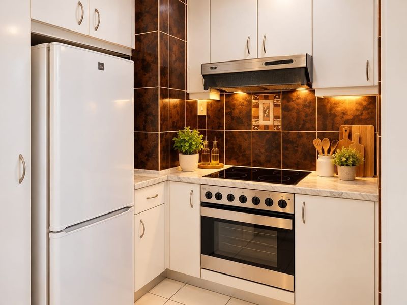 Compact kitchen featuring white cabinetry, marble-look laminate countertops, a built-in oven with electric cooktop, and a dark tiled splashback.
