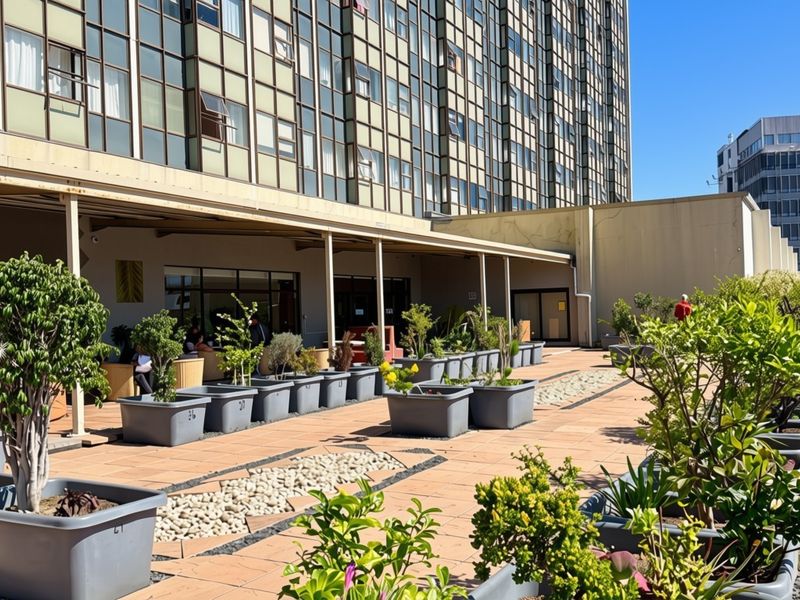 A spacious, paved outdoor patio area featuring a covered walkway and numerous potted plants, providing a pleasant communal space for residents.