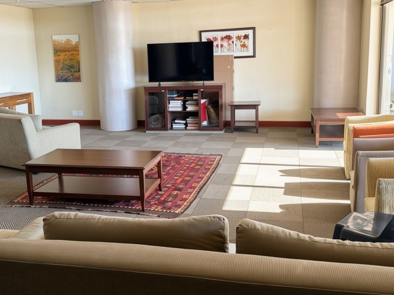 Spacious communal living area featuring neutral carpeting, structural columns, and large sliding glass doors providing access to an outdoor patio space.