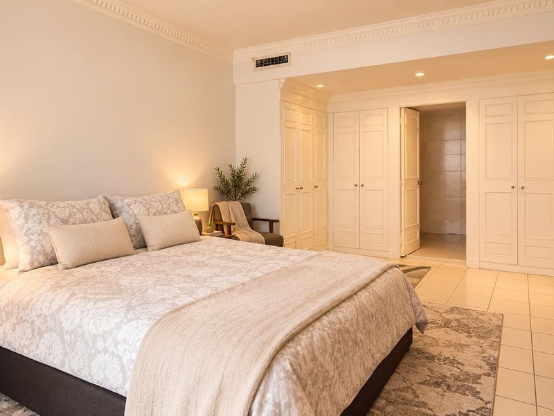 Spacious bedroom featuring built-in wardrobes, crown molding, recessed lighting, and tiled flooring, with direct access to an en-suite bathroom.