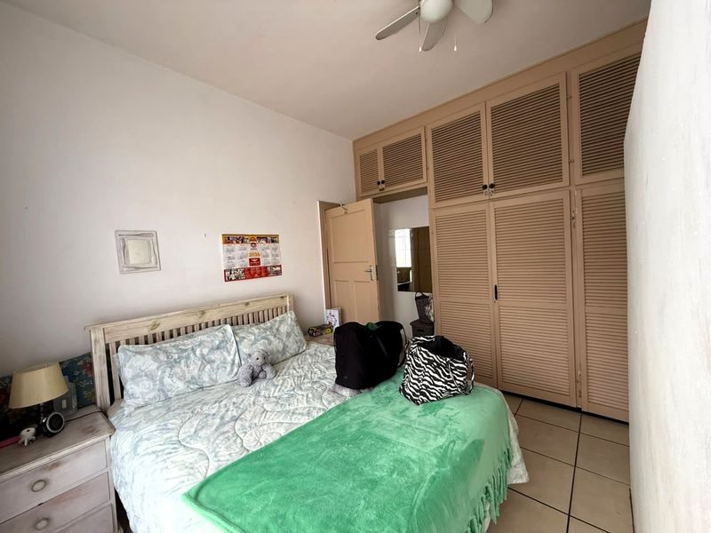 A bedroom featuring built-in louvered cupboards, a ceiling fan, and tiled flooring.