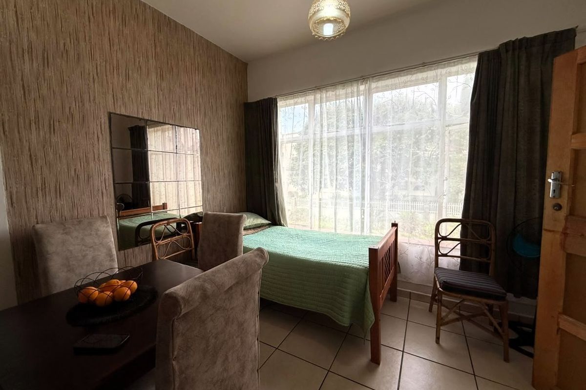 A bedroom featuring tiled flooring, textured wallpaper, and a large window with natural light, providing a functional space with a neutral aesthetic.