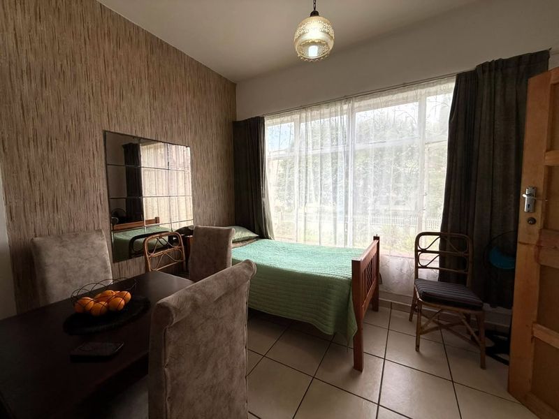 A bedroom featuring tiled flooring, textured wallpaper, and a large window with natural light, providing a functional space with a neutral aesthetic.