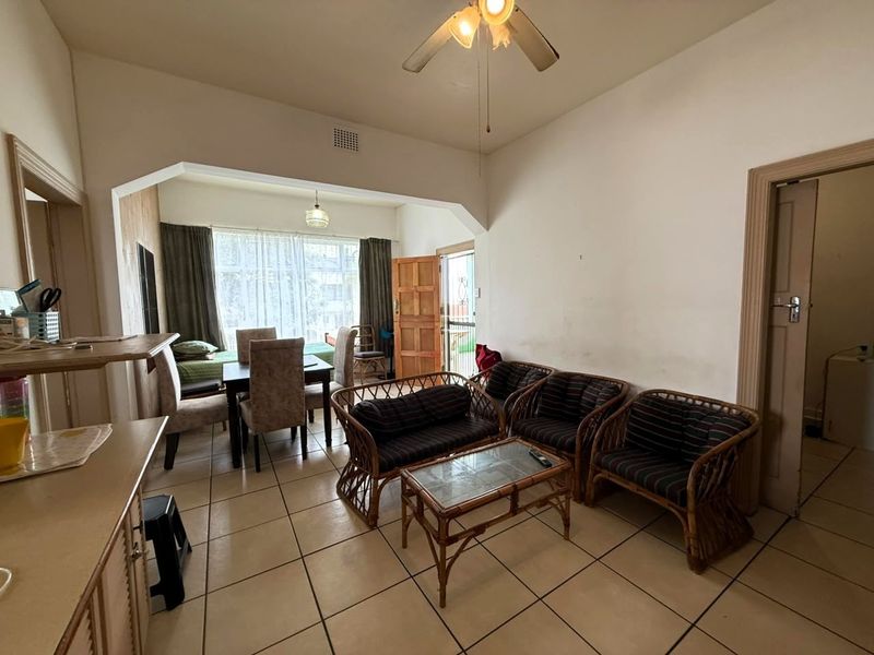 Open-plan living and dining area featuring tiled flooring, a ceiling fan, and an archway leading to a bright, naturally lit space.