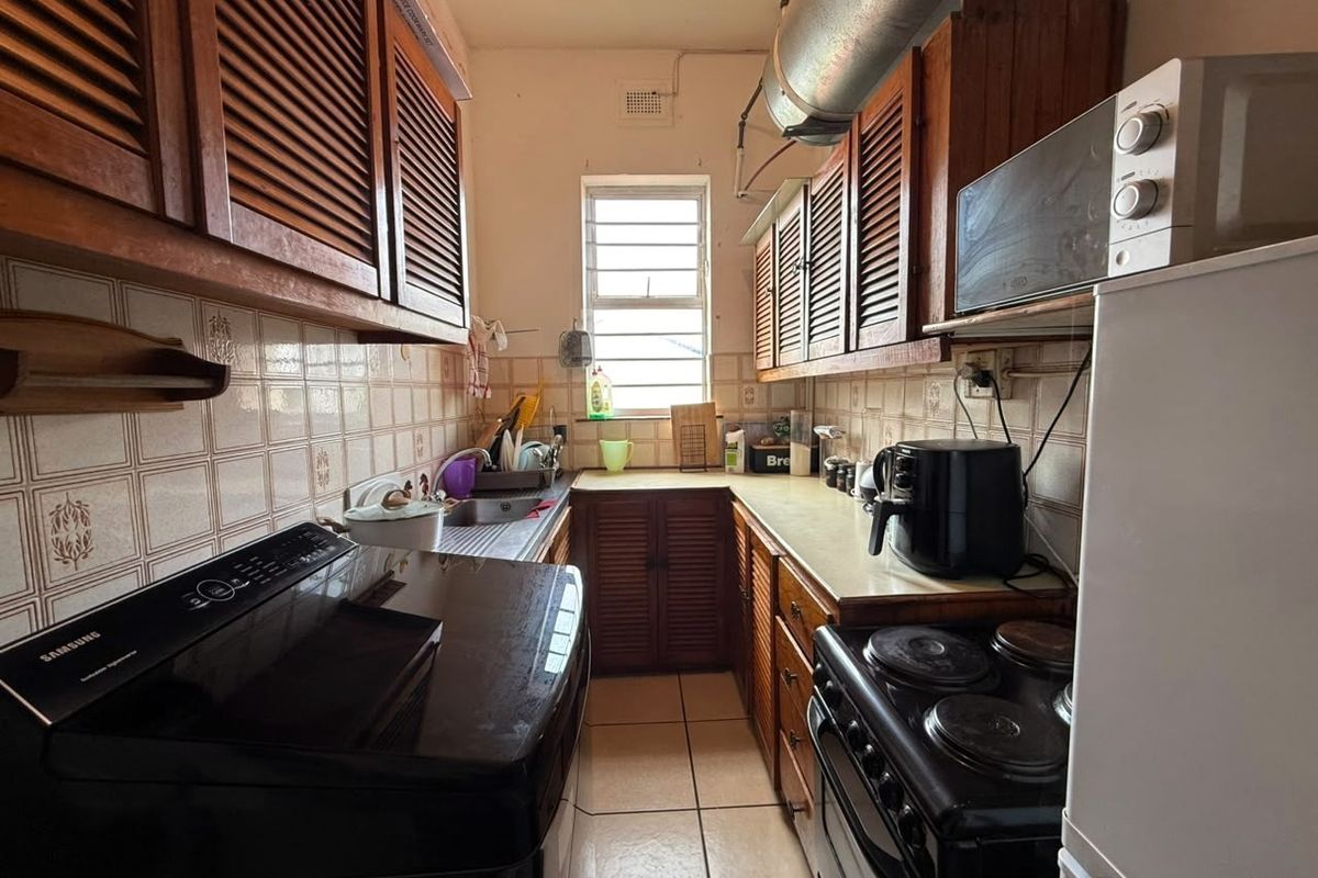 A compact galley-style kitchen featuring traditional louvered wooden cabinetry, tiled backsplash, and functional built-in appliances, offering potential for a modern renovation.