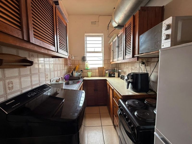 A compact galley-style kitchen featuring traditional louvered wooden cabinetry, tiled backsplash, and functional built-in appliances, offering potential for a modern renovation.