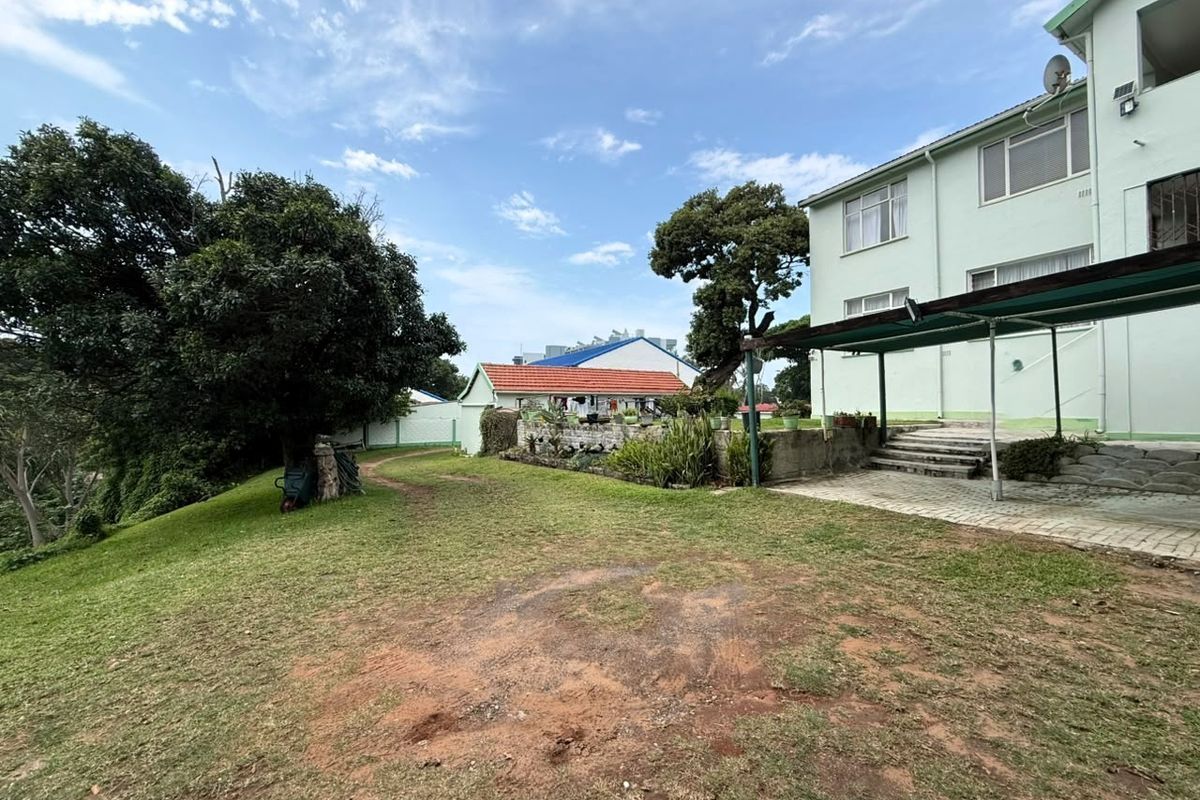 Rear exterior view of the apartment building featuring a paved patio area, covered veranda, and a spacious garden with mature trees.