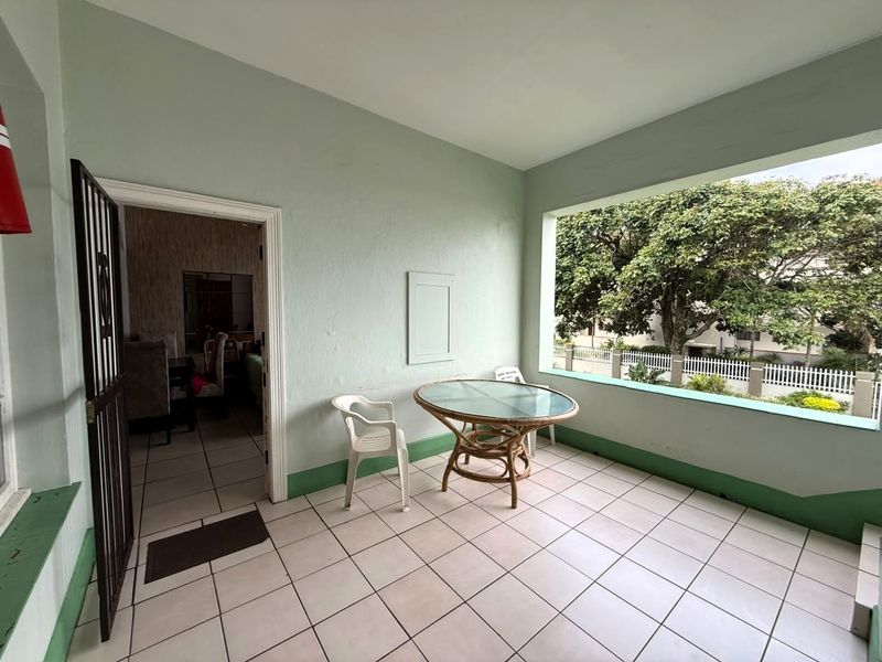 A covered balcony featuring tiled flooring and a security gate, offering an open-air space with views of the surrounding greenery.