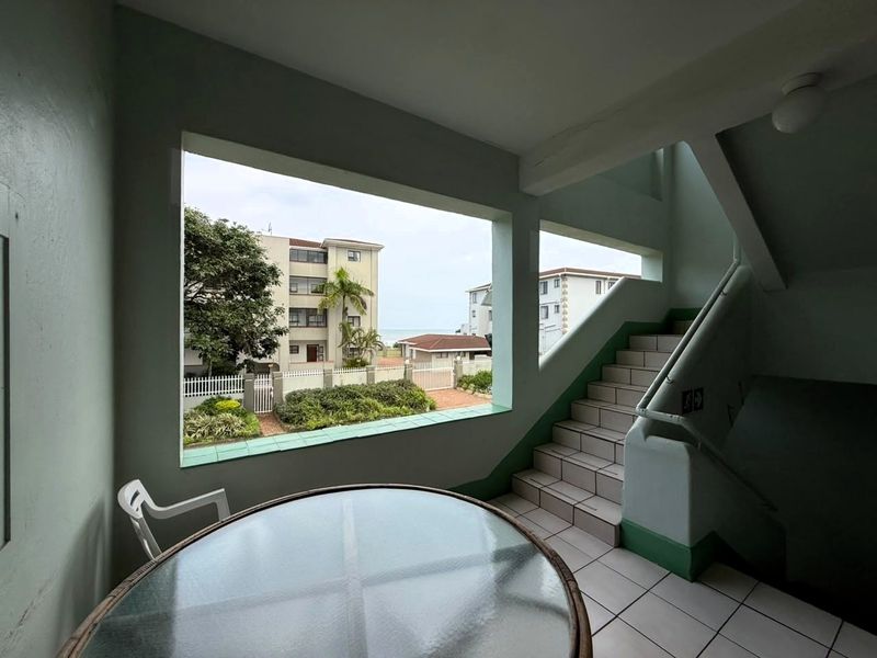 A communal stairwell area featuring tiled flooring, a handrail, and large open windows providing natural light and views of the surrounding complex.