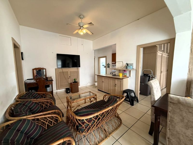 Open plan living area featuring tiled flooring, a ceiling fan, and built-in cabinetry with louvered doors, connecting to adjacent rooms through an archway.