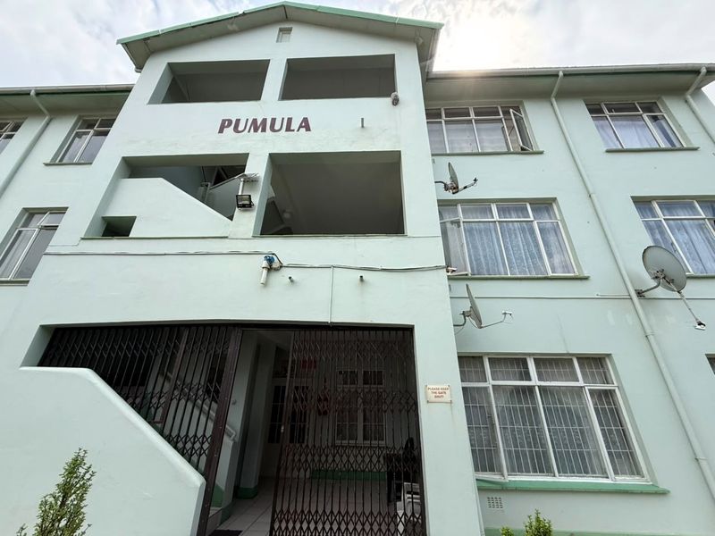 Front facade of the Pumula apartment building, featuring a gated entrance, external stairwell, and multiple window units with satellite dish installations.