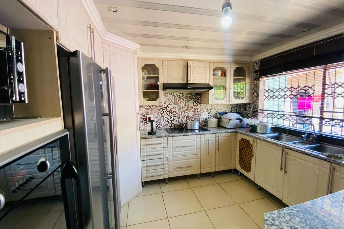 A functional kitchen featuring granite countertops, mosaic tile backsplash, built-in cabinetry, and a stainless steel double sink with security window bars.