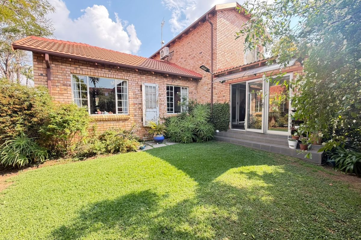 Rear view of a face brick house featuring a well-maintained lawn, tiled patio area, and sliding glass doors providing access to the interior.