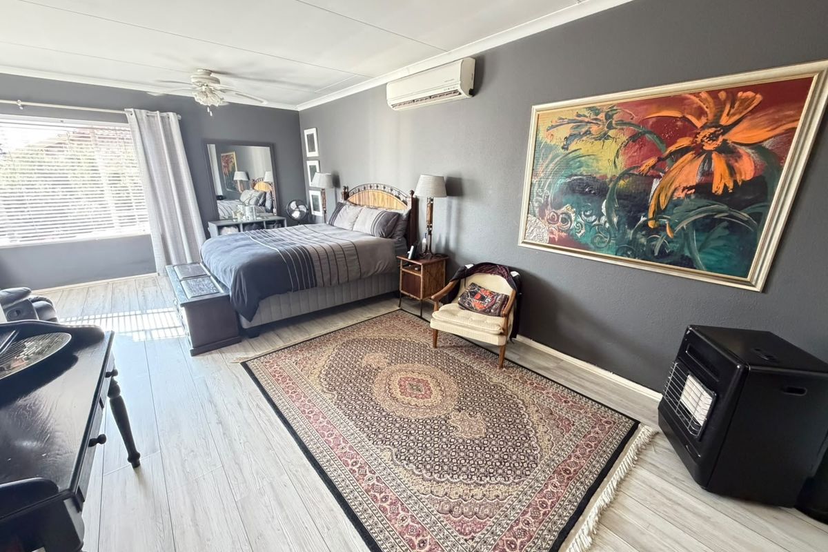Spacious bedroom featuring light-toned laminate flooring, a ceiling fan, and a wall-mounted split-system air conditioning unit.