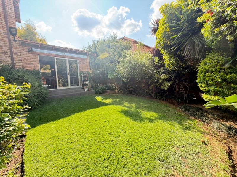 A well-maintained rear garden featuring a lush green lawn, mature landscaping, and direct access to the home via sliding glass doors.