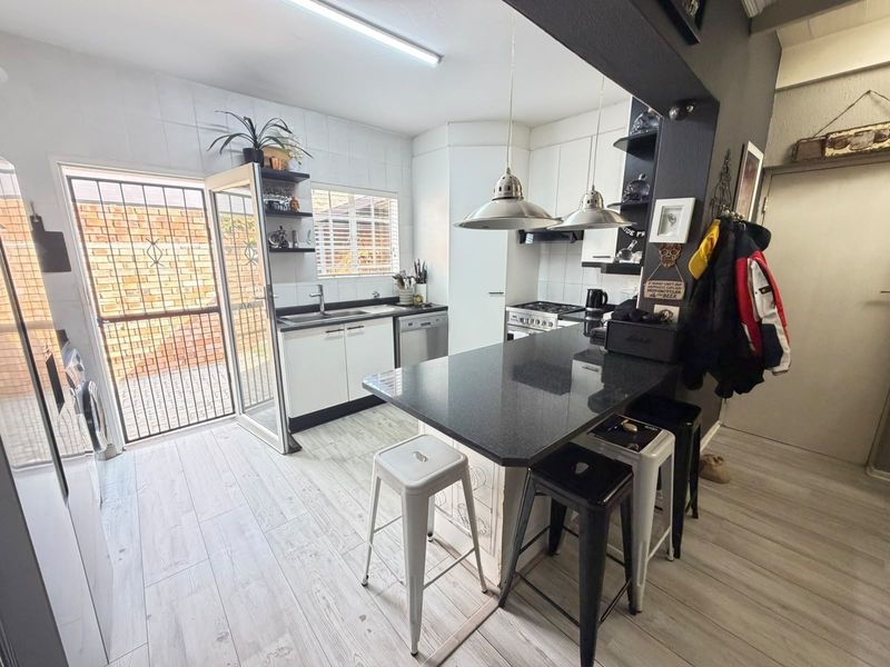 Modern kitchen featuring a central island with granite countertops, built-in oven, hob, extractor fan, and direct access to an outdoor area via a security gate.