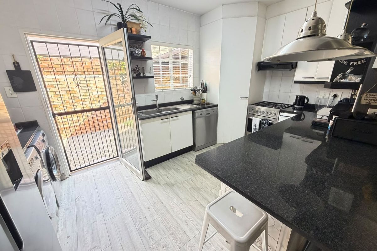 Modern kitchen featuring granite countertops, gas stove, extractor fan, and direct access to an outdoor area through a secure door.