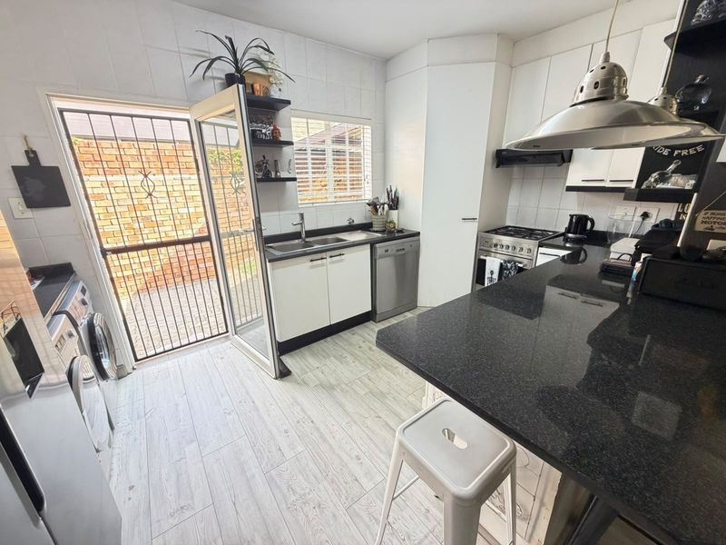 Modern kitchen featuring granite countertops, gas stove, extractor fan, and direct access to an outdoor area through a secure door.