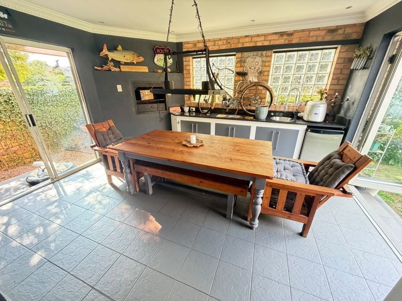 Enclosed patio area featuring a built-in braai, kitchenette with sink, exposed brickwork, and large sliding doors providing access to the garden.