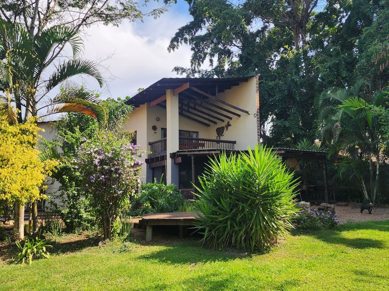 Rear view of the property featuring a multi-level design with a timber balcony, exposed rafters, and a well-maintained garden with a wooden deck.
