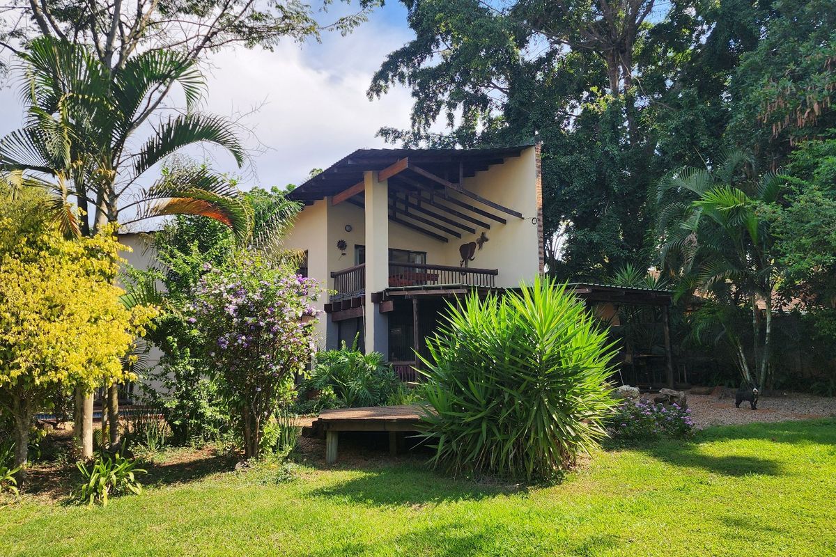 Rear view of the property featuring a multi-level design with a timber balcony, exposed rafters, and a well-maintained garden with a wooden deck.
