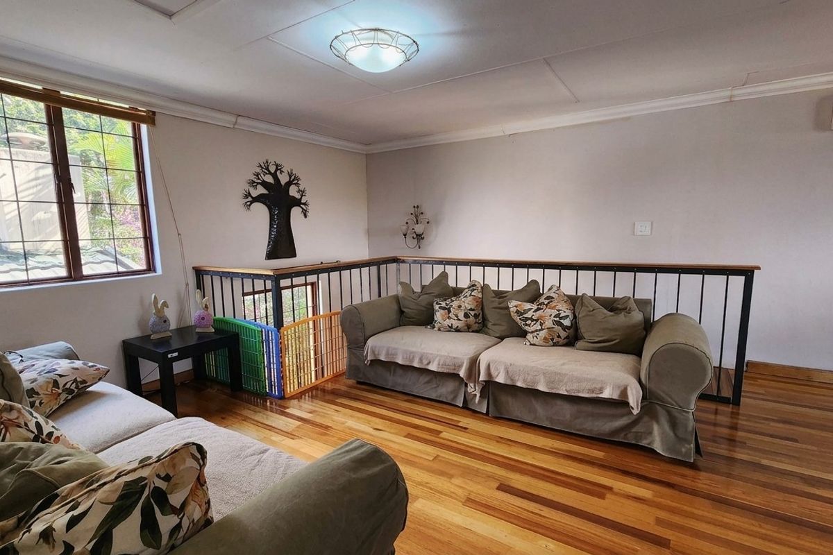 A living area featuring polished hardwood flooring, a metal balustrade overlooking the lower level, and a wall-mounted air conditioning unit.