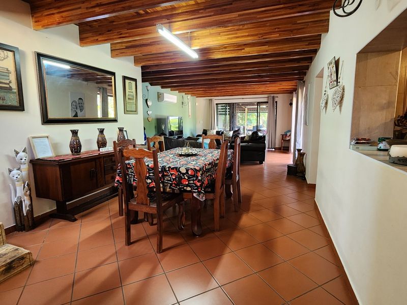 Spacious open-plan living and dining area featuring exposed timber beam ceilings, terracotta floor tiles, and direct access to the outdoor patio through sliding glass doors.