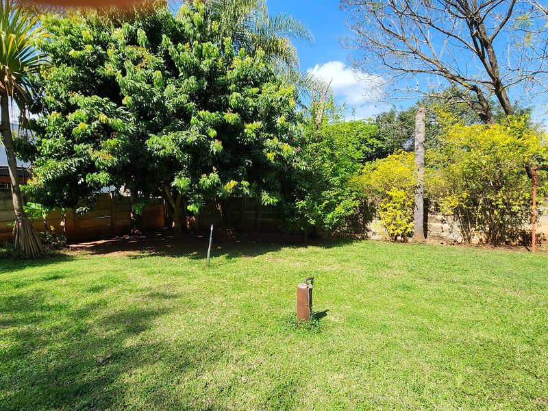 A spacious private garden featuring a well-maintained lawn, mature trees, and secure precast concrete boundary walling.