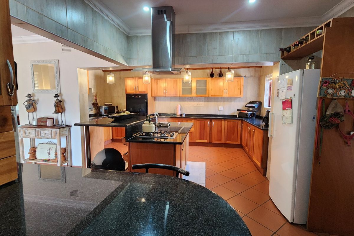 Spacious kitchen featuring wooden cabinetry, granite countertops, a central island with a gas hob, and a stainless steel extractor fan.