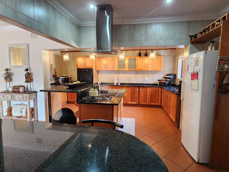 Spacious kitchen featuring wooden cabinetry, granite countertops, a central island with a gas hob, and a stainless steel extractor fan.