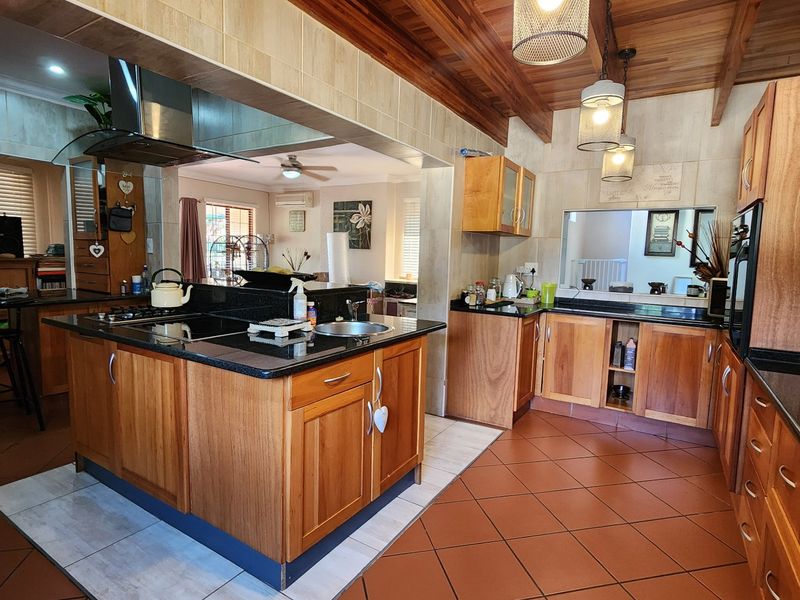 Spacious open-plan kitchen featuring warm wooden cabinetry, granite countertops, a central island, and exposed timber ceiling beams, seamlessly flowing into the living area.