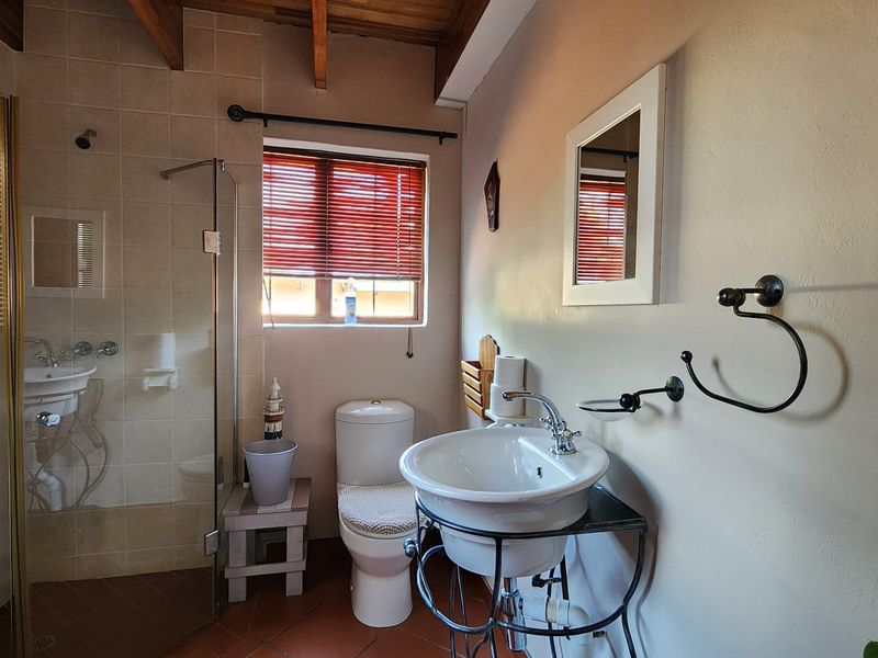 A functional bathroom featuring a glass-enclosed shower, pedestal basin, toilet, and exposed timber ceiling beams, finished with tiled flooring.