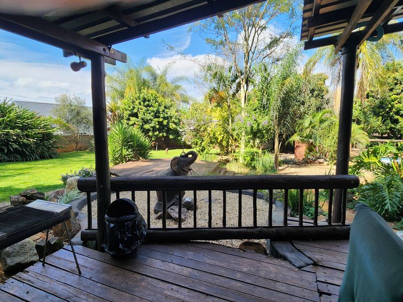 Covered timber patio overlooking a lush garden with mature trees and landscaped lawn area.