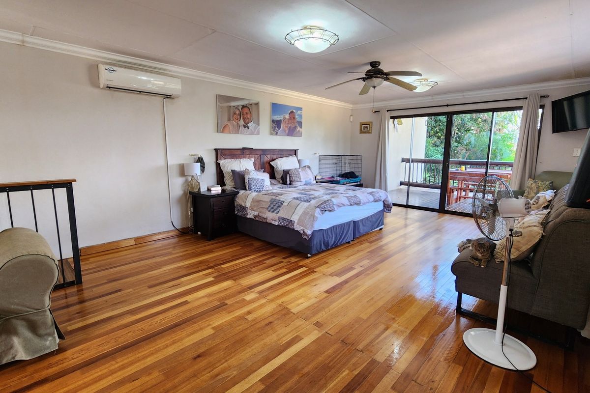 Spacious bedroom featuring polished hardwood flooring, a ceiling fan, split-system air conditioning, and sliding glass doors leading to an outdoor balcony.