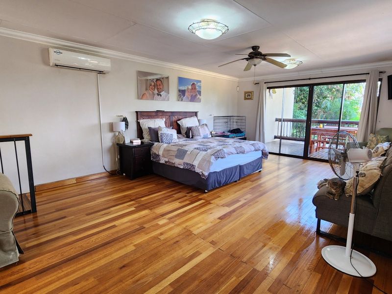 Spacious bedroom featuring polished hardwood flooring, a ceiling fan, split-system air conditioning, and sliding glass doors leading to an outdoor balcony.