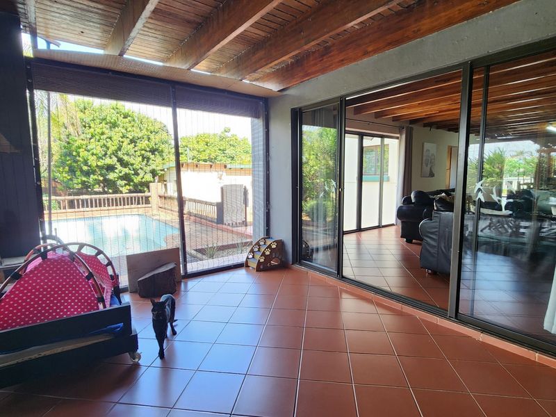 Covered patio area featuring exposed timber beam ceilings, tiled flooring, and large sliding glass doors providing seamless access to the interior living space.