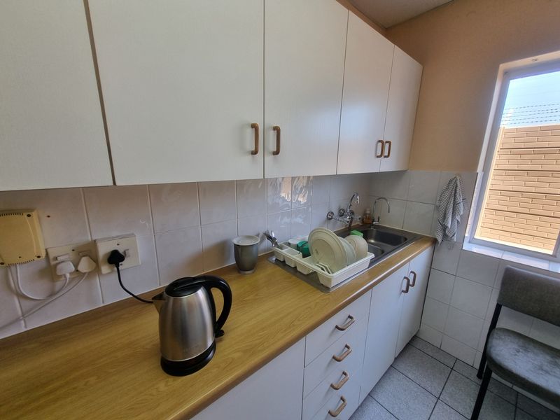 A functional kitchenette featuring white cabinetry, a laminate countertop, a stainless steel sink, and tiled finishes.