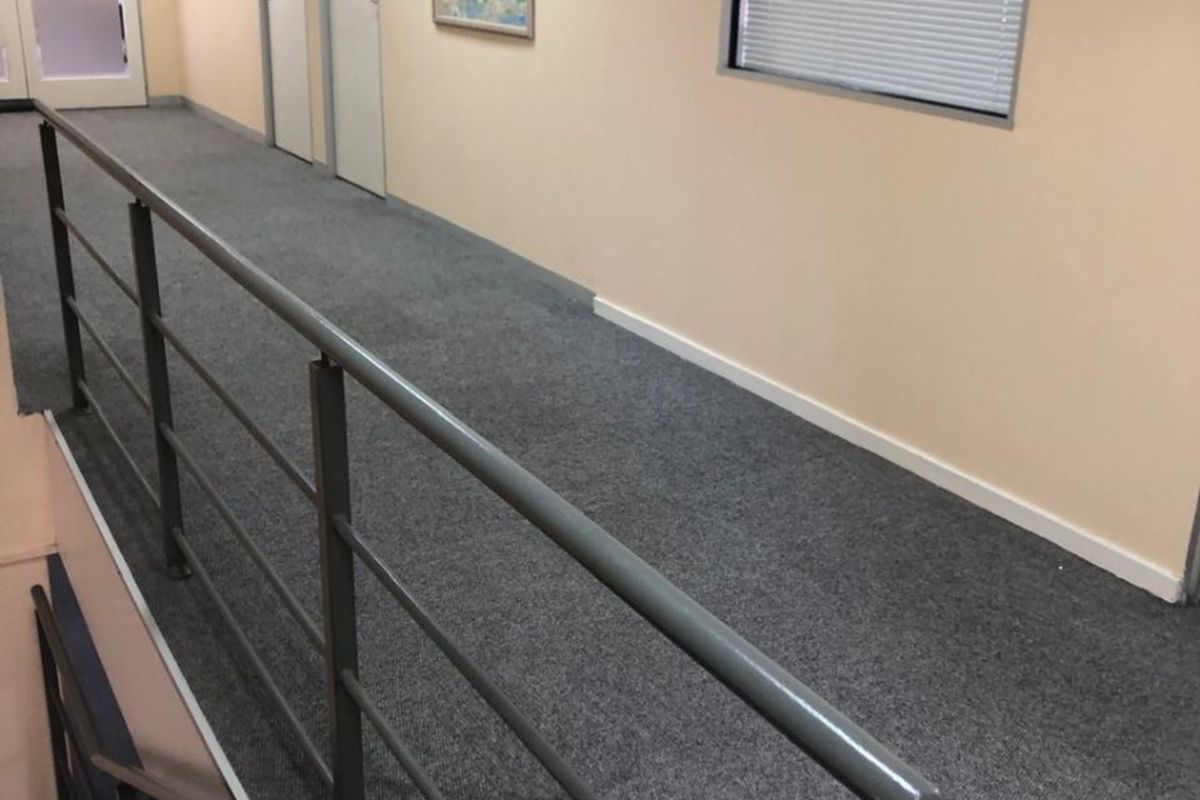 A functional office hallway featuring grey carpeting, a metal safety balustrade overlooking the staircase, and multiple internal office doors.