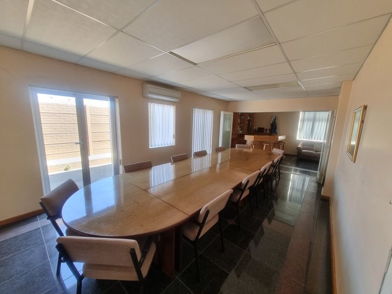 Spacious office area featuring tiled flooring, suspended ceiling, split-system air conditioning, and natural light through vertical blinds and a glass sliding door.