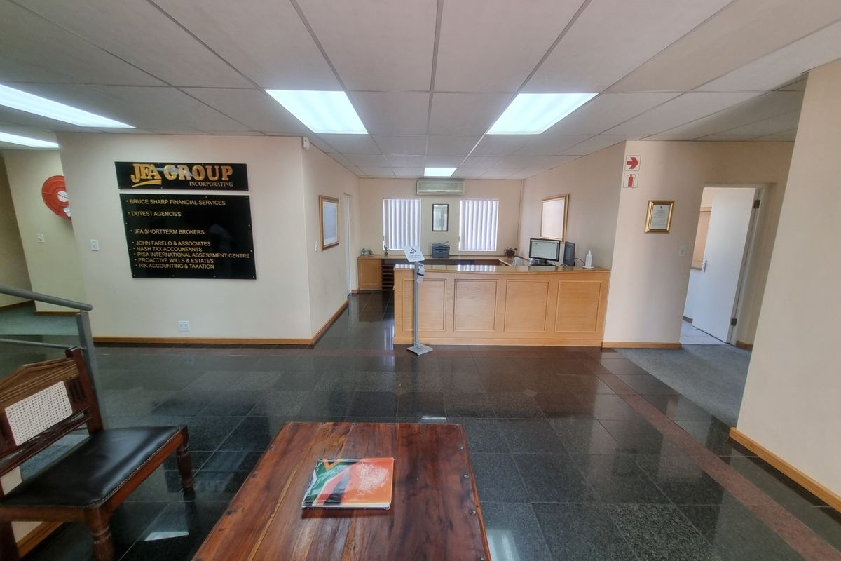 A professional office reception area featuring a built-in wooden reception desk, polished tile flooring, and integrated lighting within a suspended ceiling.