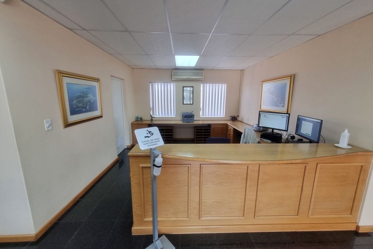 Professional office reception area featuring a built-in wooden desk, suspended ceiling, air conditioning, and vertical blinds.