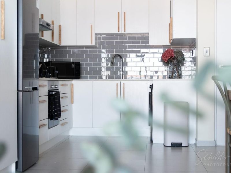 Modern kitchen featuring white cabinetry, grey subway tile backsplash, integrated appliances, and sleek fixtures, offering a clean and contemporary aesthetic.