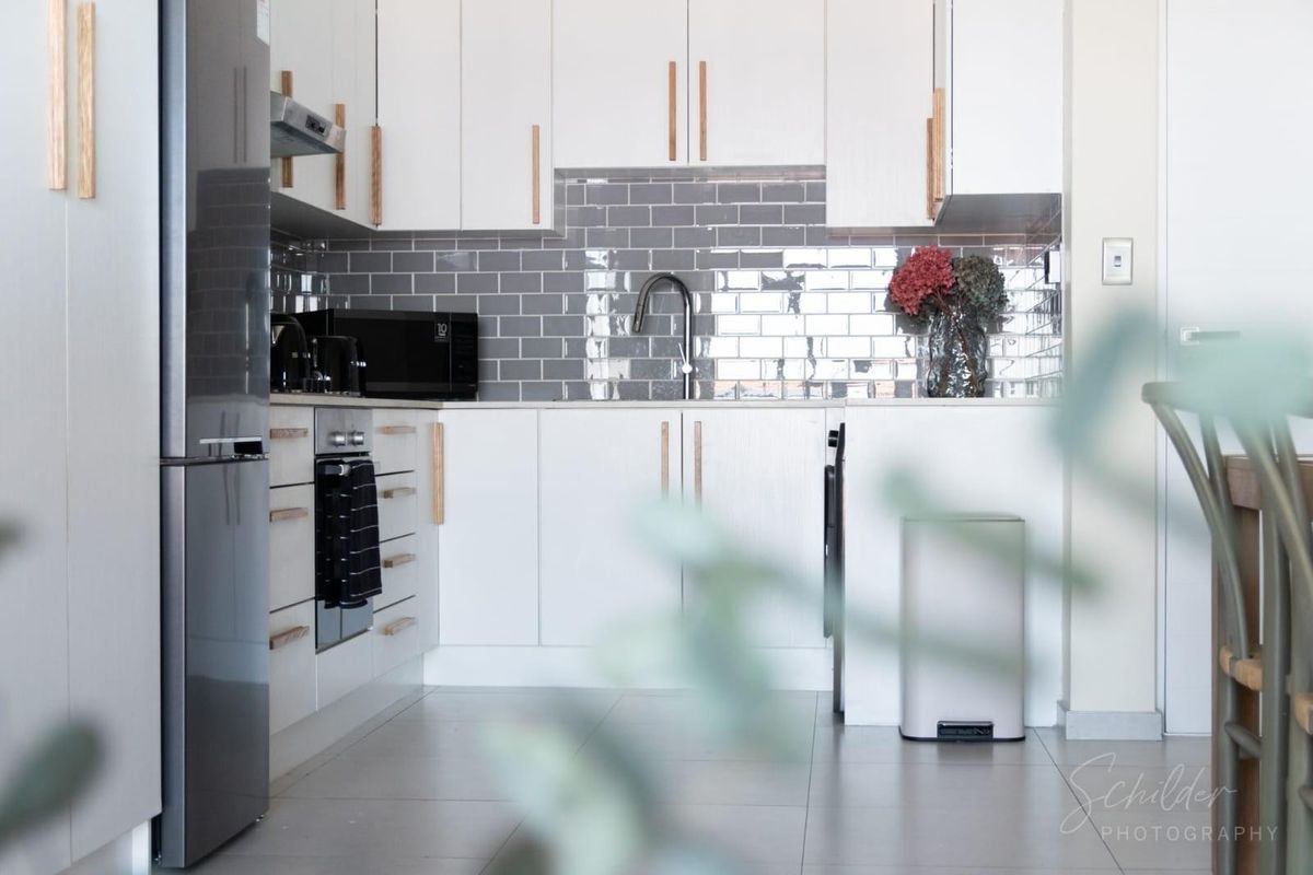 Modern kitchen featuring white cabinetry, grey subway tile backsplash, integrated appliances, and sleek fixtures, offering a clean and contemporary aesthetic.