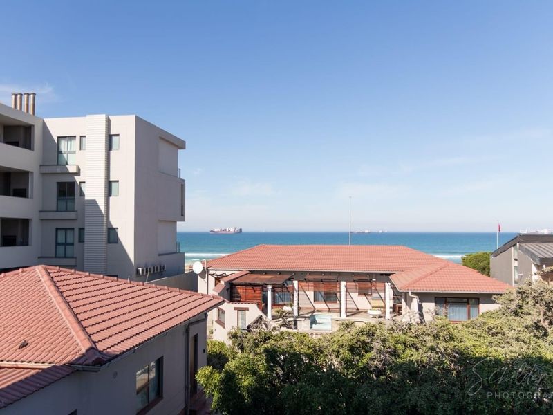 Elevated view overlooking neighboring residential rooftops with a clear perspective of the ocean and coastline.